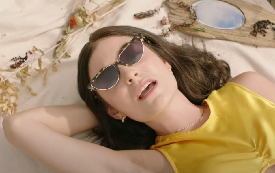 New Zealand Singer Lorde lying back wearing sunglasses and a yellow dress