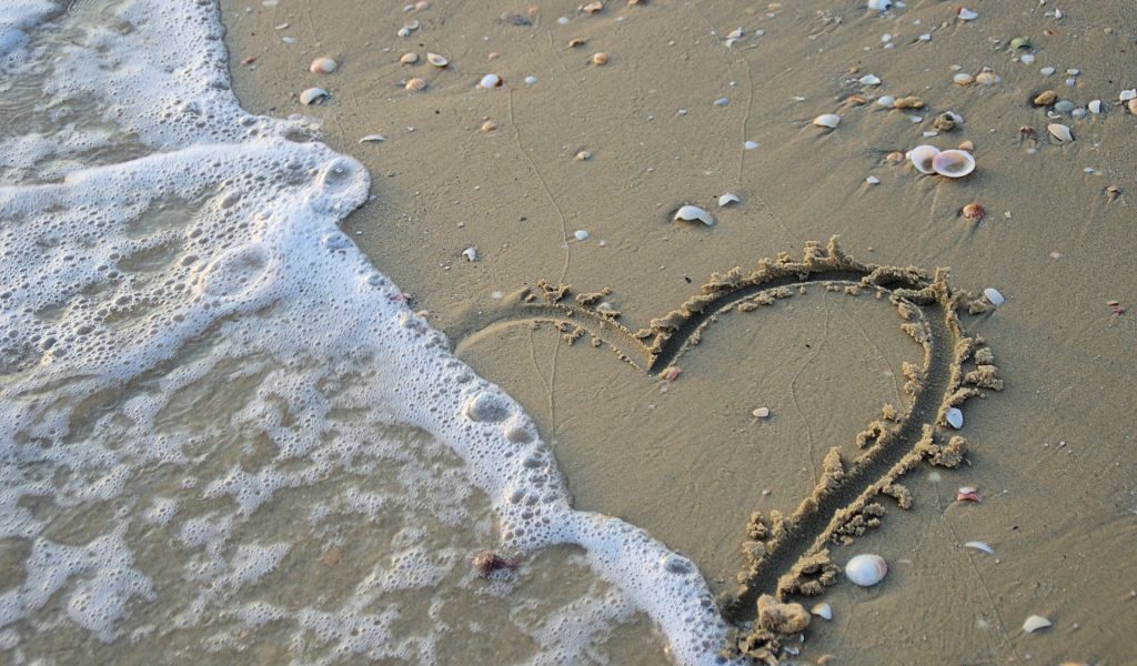 Wave washing out a heart drawn in the sand