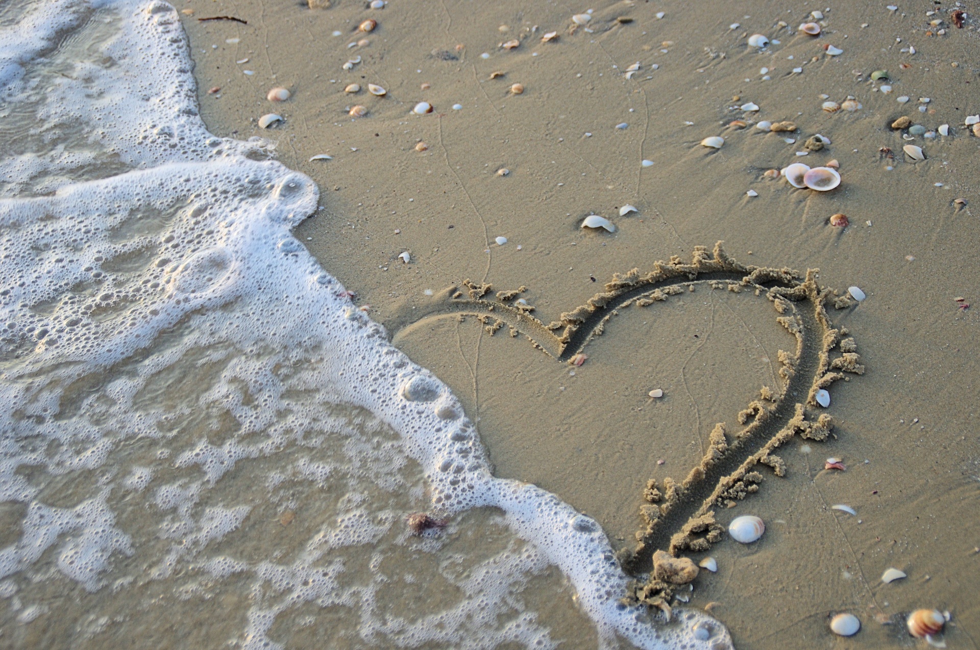Wave washing out a heart drawn in the sand
