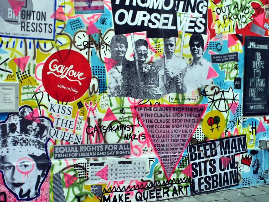 Queer graffiti in Brighton includes the repeated phrase 'Stop the clause' in a triangle, 'Equal rights for all, fight for lesbian and gay rights', 'Kiss the Queen' with a photo of young Queen Elizabeth, 'Gay Love it's the real thing' in a red circle and 'Make queer art' at the bottom.